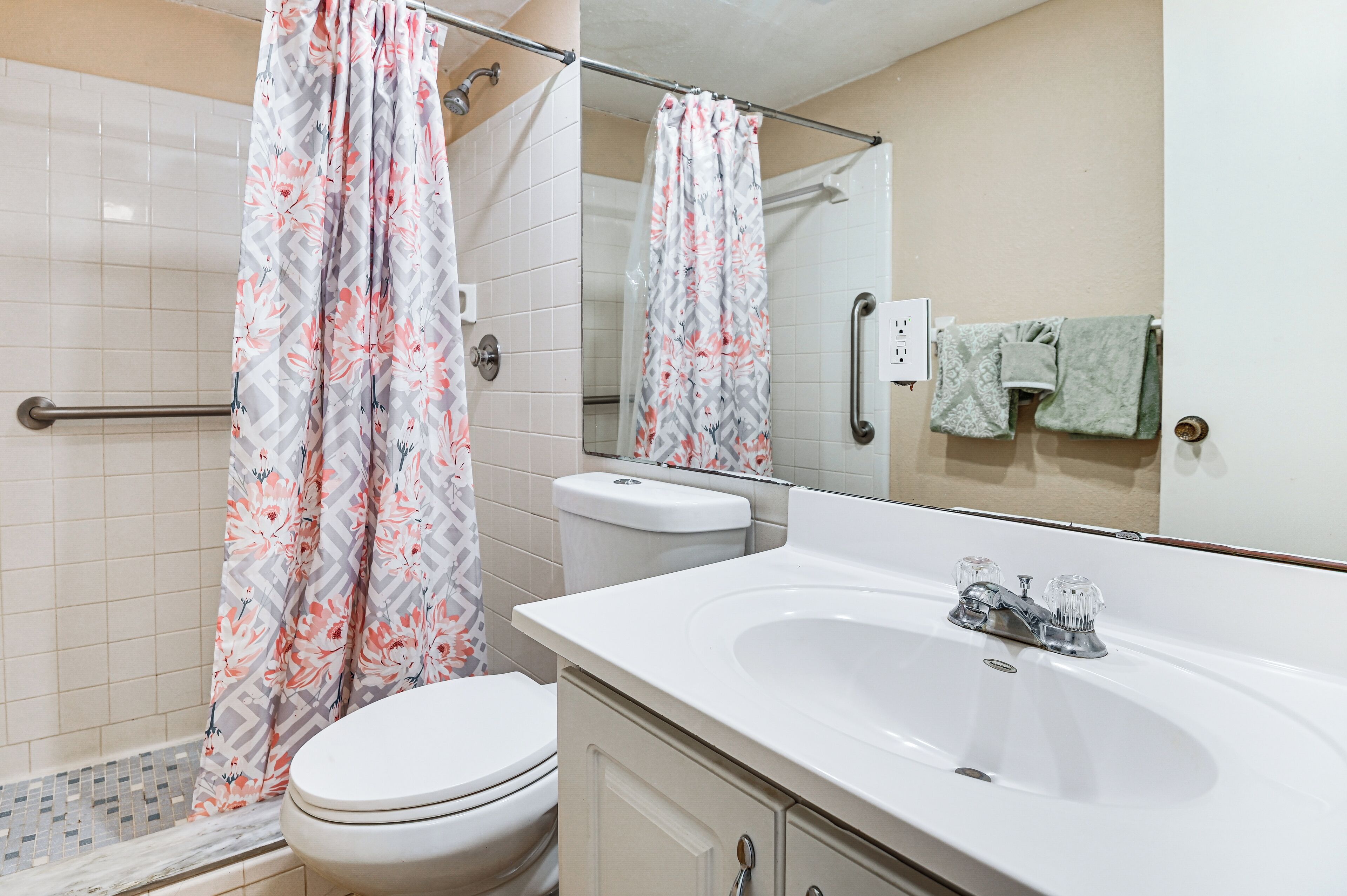 A bathroom with a shower, toilet, sink, and a mirror.