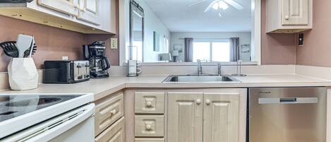 A modern kitchen with a dishwasher, stove, and a large mirror above the sink.