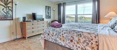 A bedroom with a bed, dresser, television, and a window with curtains.