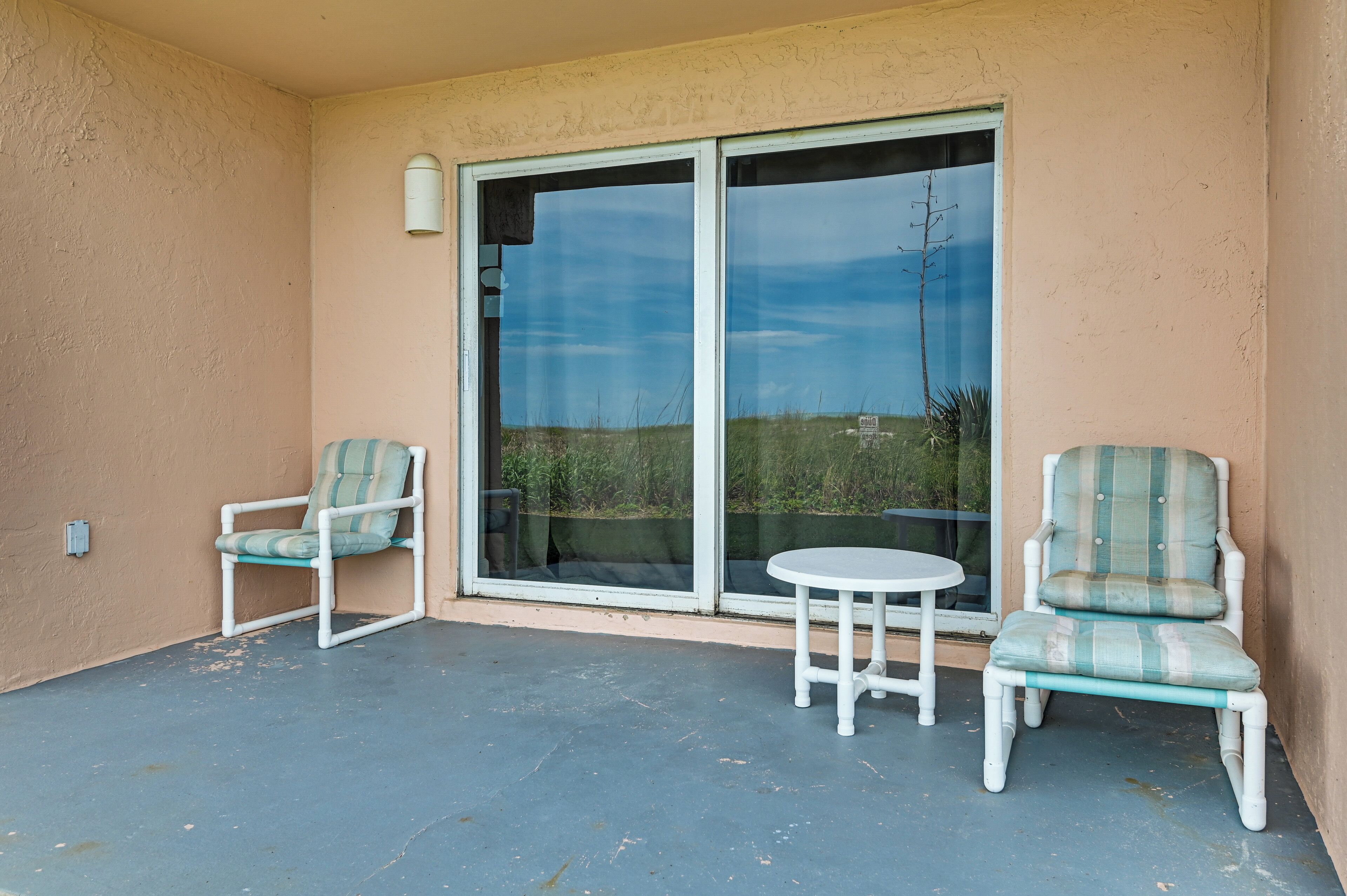 Un balcon avec deux chaises et une petite table, une porte-fenêtre coulissante et un luminaire fixé au mur.