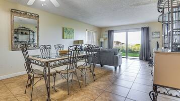 Un espace repas avec une table en verre et des chaises en métal, un canapé, un grand miroir et une vue sur l’extérieur.