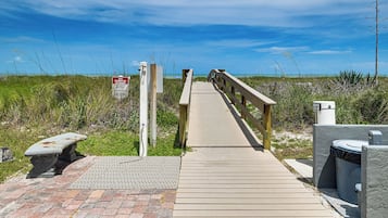 Une promenade en bois menant à une plage, avec un panneau indiquant qu’il est interdit de se garer sur la plage.