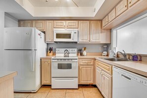 A kitchen with wooden cabinets, a refrigerator, a microwave, an oven, a dishwasher, and a sink. - Ocean-view Balcony & Pool Access! Cocoa Beach Gem (Cocoa Beach)