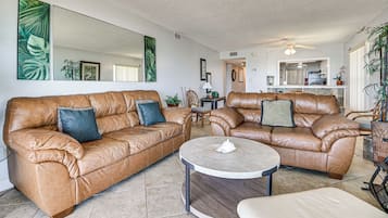 A spacious living room with two leather sofas, a round coffee table, and a large mirror on the wall.