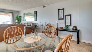 Un comedor con mesa de vidrio, sillas de mimbre, sofá de cuero y una consola decorada con objetos ornamentales.