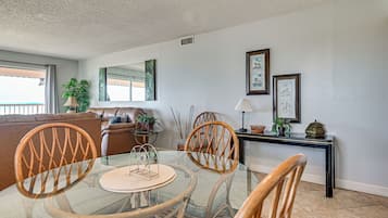 A dining area with a glass table, wicker chairs, a leather sofa, and a console table with decorative items.