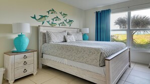 A bedroom with a bed, two bedside tables, a window with curtains, and wall art. - Enjoy the Pool & Beach! Cocoa Beach Condo (Cocoa Beach)