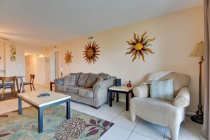 Ein Wohnzimmer mit einer Couch, Sesseln, einem Couchtisch und Wandkunst mit Sonnenmotiv.