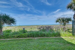 A grassy area with palm trees and a view of the ocean. - Walkable Cocoa Beach Condo w/ Ocean Views (Cocoa Beach)