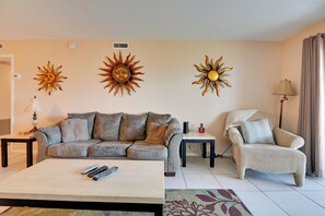 Ein Wohnzimmer mit einer Couch, einem Sessel, einem Couchtisch und Sonnendekoration an der Wand.