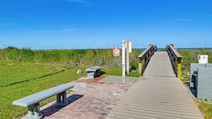 A wooden boardwalk leading to beach access, with a bench and a signpost. - Enjoy the Pool & Beach! Cocoa Beach Condo (Cocoa Beach)