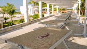 A row of sun loungers under white umbrellas, with a view of palm trees and buildings in the background. - Room 'Casale San Giovanni - Camera 2' with Shared Terrace, Wi-Fi and Air Conditioning (Salice Salentino)