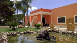 A building with a red facade, a covered entrance, and a small pond with rocks. - Room 'Casale San Giovanni - Camera 2' with Shared Terrace, Wi-Fi and Air Conditioning (Salice Salentino)