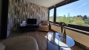 A modern living room with a television, a sofa, a glass coffee table, and a large window offering a view of greenery. - Eifel Pearl Manderscheid 2 (Manderscheid)