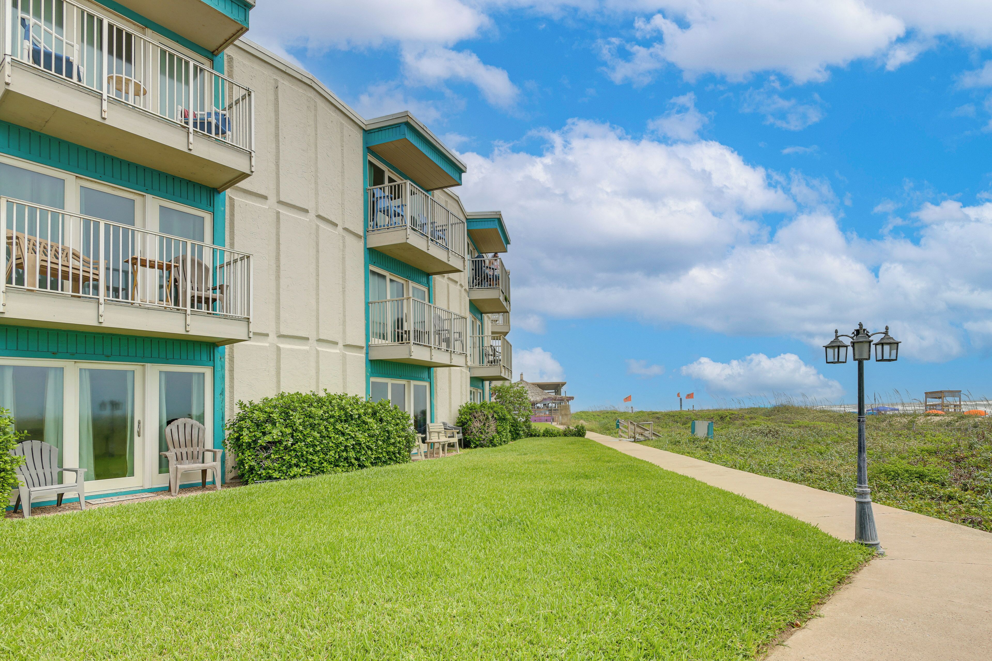 A multi-story building with balconies, a grassy lawn, and a clear sky.