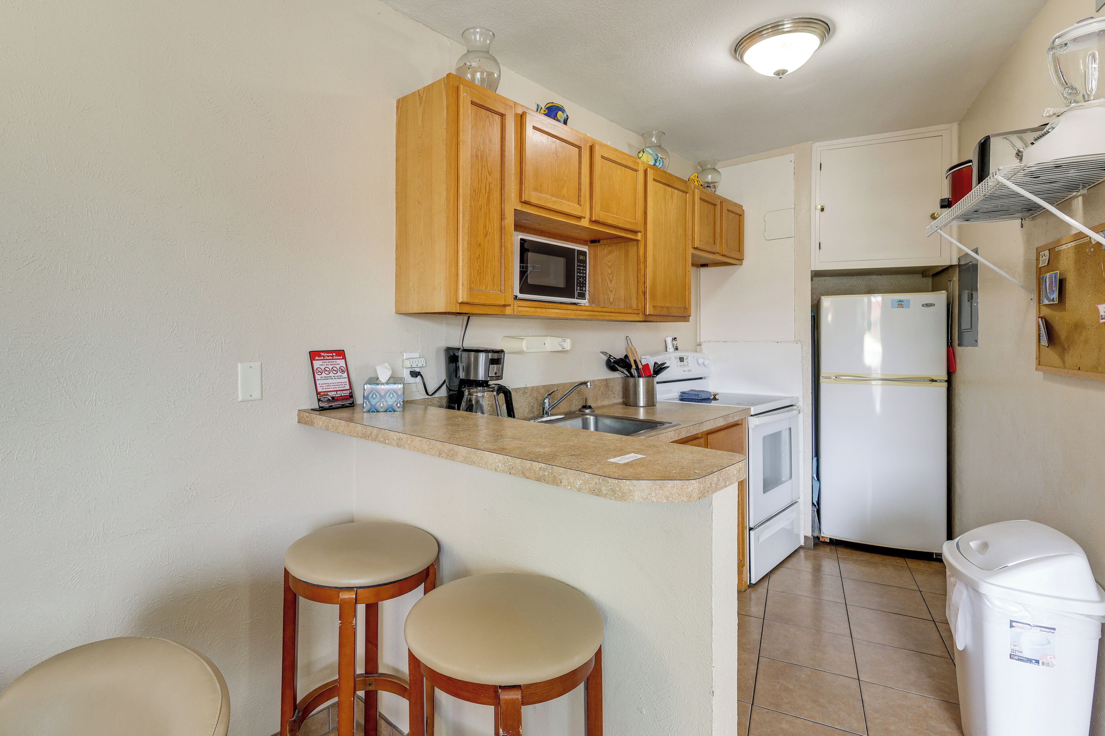 A kitchen with wooden cabinets, a microwave, a refrigerator, and a small island with stools.