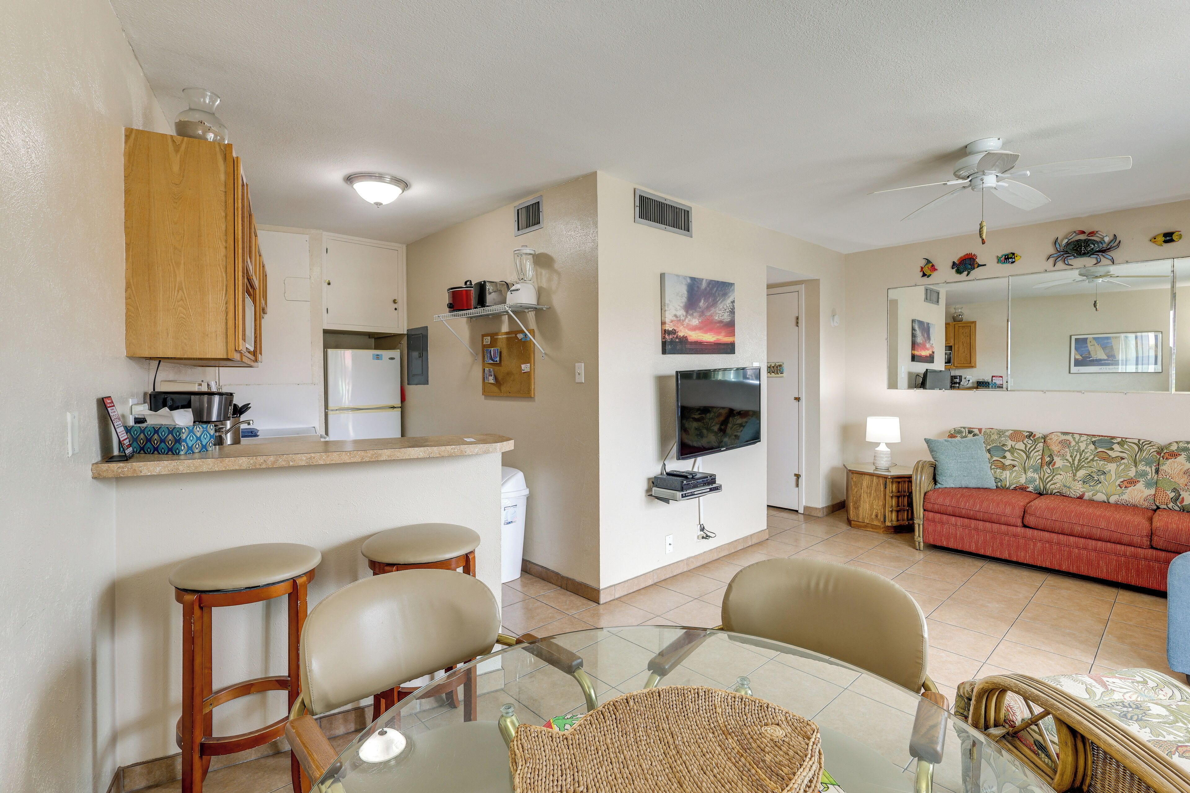Een compacte leefruimte met een kitchenette, een eethoek met een glazen tafel, een bank en een aan de muur bevestigde televisie.