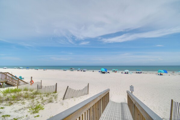 A beach with a wooden walkway leading to the water, umbrellas, and beach chairs. - Walk to Beach! Water-view Home in Gulf Shores (Gulf Shores)