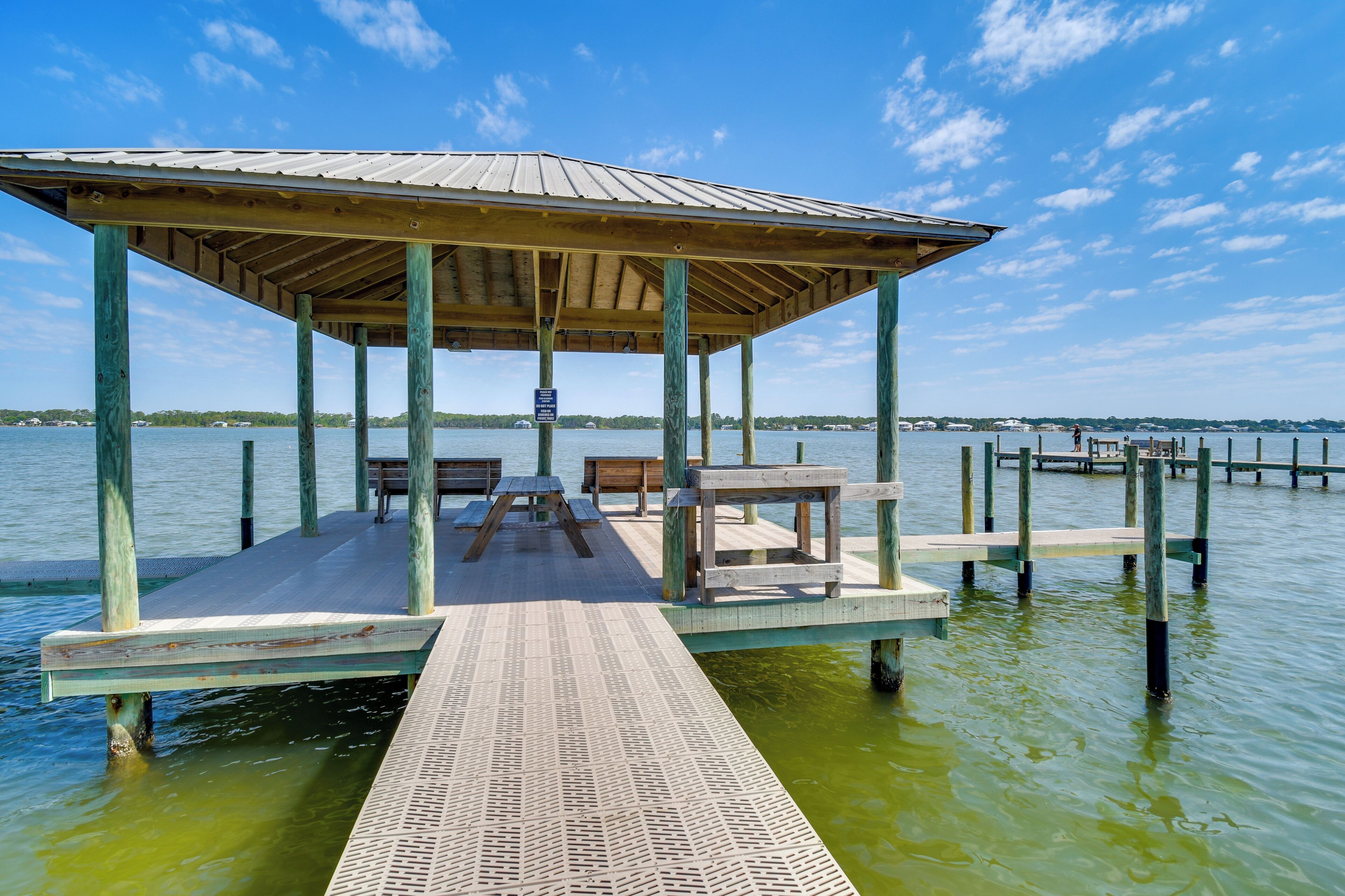 A wooden pier with a covered seating area, benches, and a picnic table.