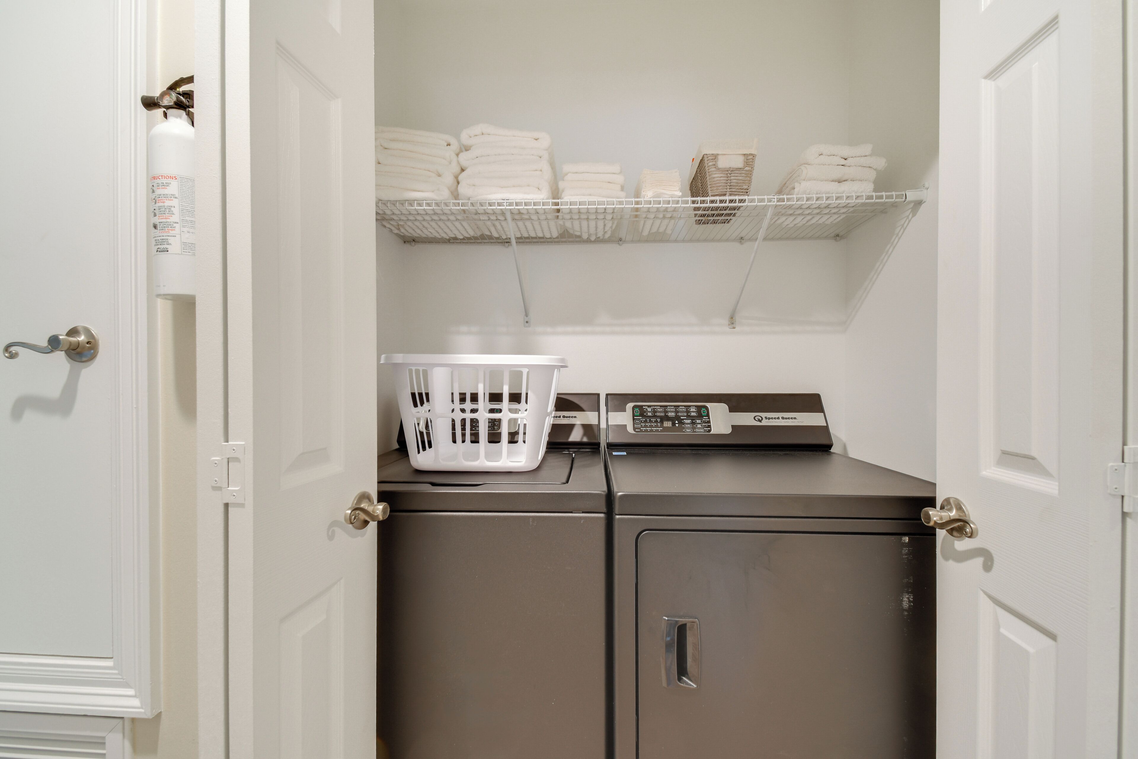 A laundry room with a washing machine, a dryer, a shelf with folded towels, and a basket.