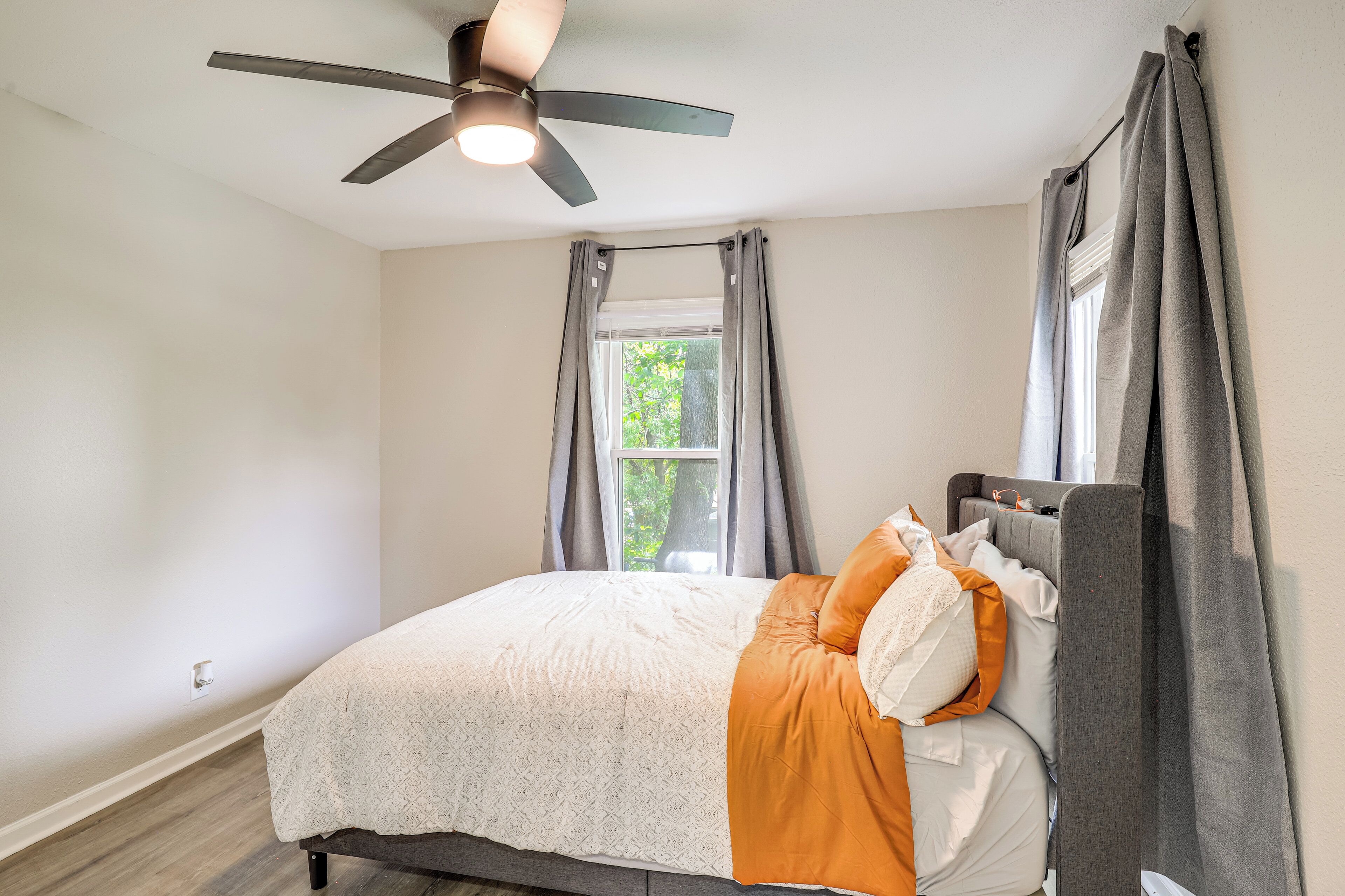 Un dormitorio con cama, ventilador de techo, ventana con cortinas y vistas al exterior.
