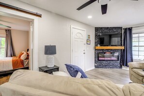 A bedroom with a bed, a nightstand, a lamp, a TV, a fireplace, and a view of the outdoors. - Game-day Getaway Near Arrowhead Stadium & Casinos! (Kansas City)