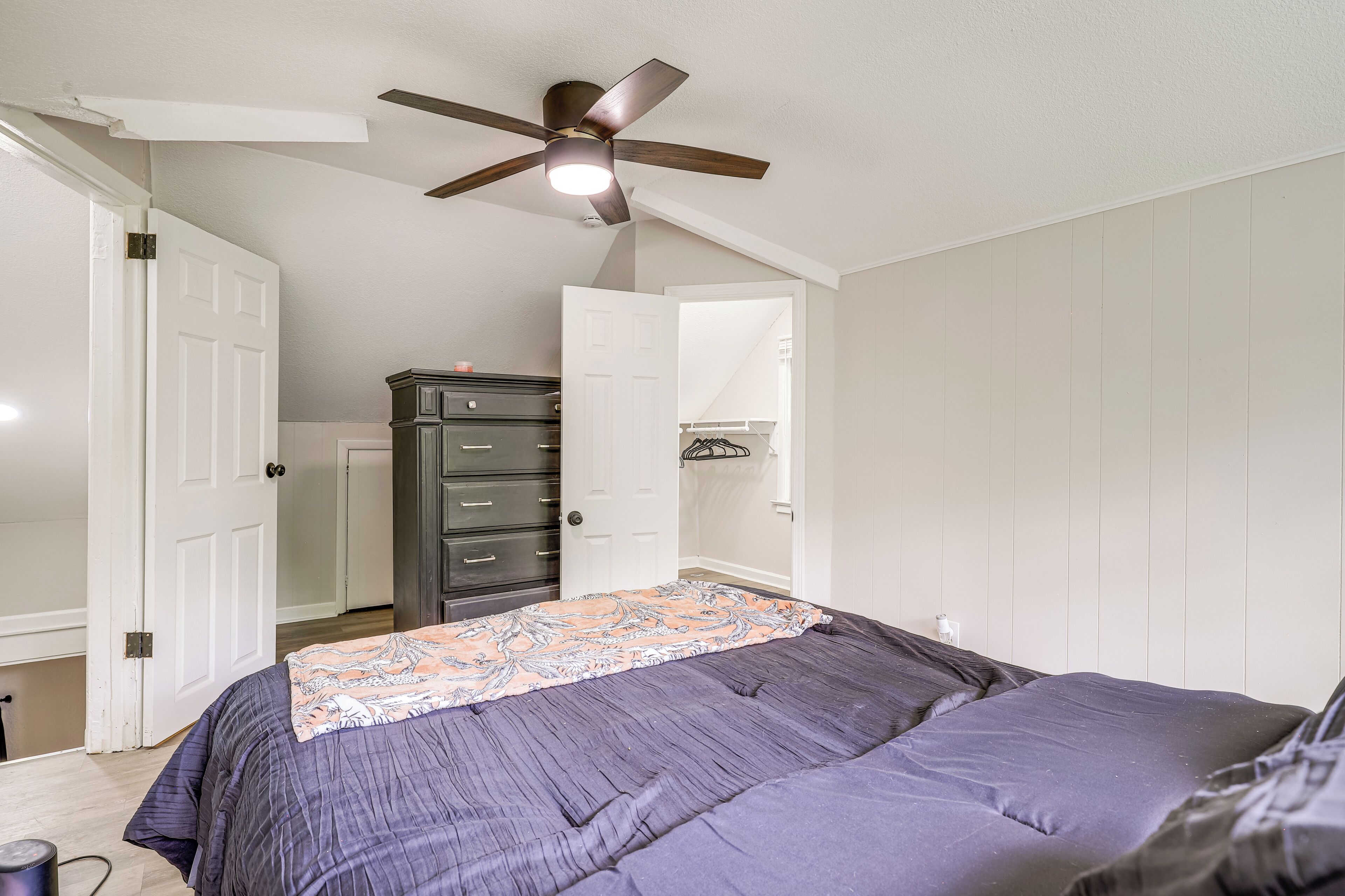 Un dormitorio con cama, ventilador de techo, cómoda y puerta que da a otra habitación.