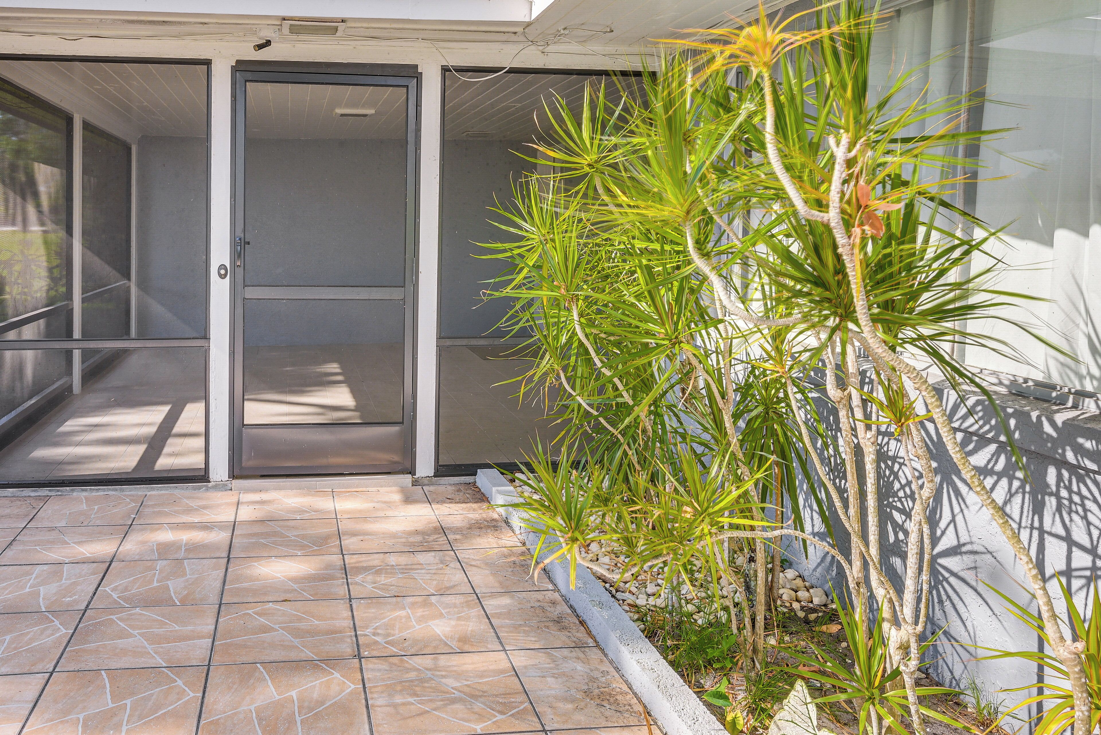 A covered outdoor area with a tiled floor, a door, and a plant with long green leaves.