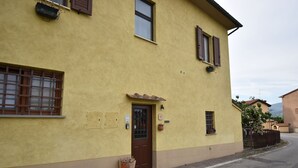 A yellow building with a brown door, windows with shutters, and a small garden area. - Comfortable and welcoming apartment (Anghiari)