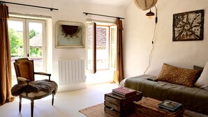 A room with a chair, a sofa, a radiator, a hanging light fixture, and a painting on the wall. - Au Canari, a former bar-tabac transformed into a charming gîte in the village of Colette. (Saint-Sauveur-en-Puisaye)
