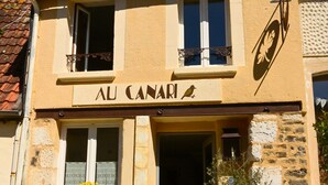 A two-story building with a sign reading 'AL CANARI' and a bird logo. There are two windows with white frames and a door with a small step leading to the entrance. - Au Canari, a former bar-tabac transformed into a charming gîte in the village of Colette. (Saint-Sauveur-en-Puisaye)