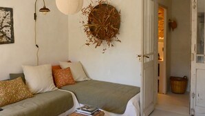 A cozy room with a bed, a sofa, a wall-mounted lamp, and a decorative wall piece. - Au Canari, a former bar-tabac transformed into a charming gîte in the village of Colette. (Saint-Sauveur-en-Puisaye)