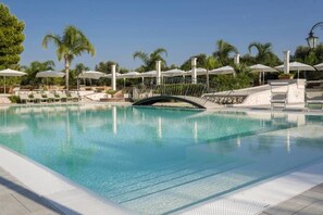 Une piscine entourée de palmiers, avec des chaises longues et des parasols.