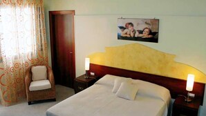 Una habitación de hotel con una cama, una silla, una mesita de noche, una lámpara y un cuadro colgado en la pared.