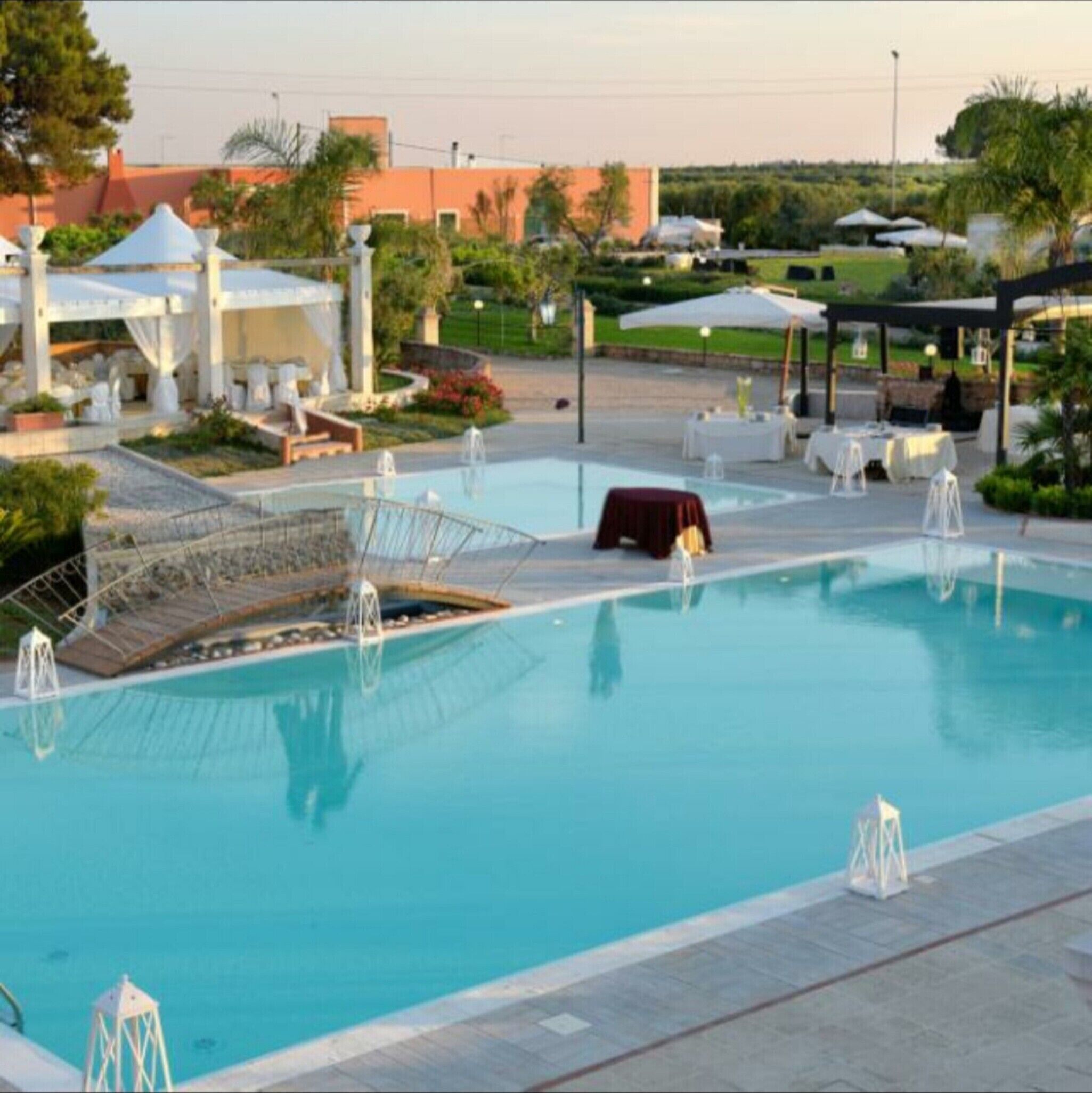 A swimming pool with lounge chairs and umbrellas, surrounded by a landscaped garden and buildings in the background.
