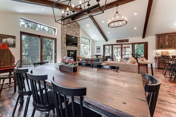 A spacious living area with a large wooden table, black chairs, a fireplace, and a stone wall.