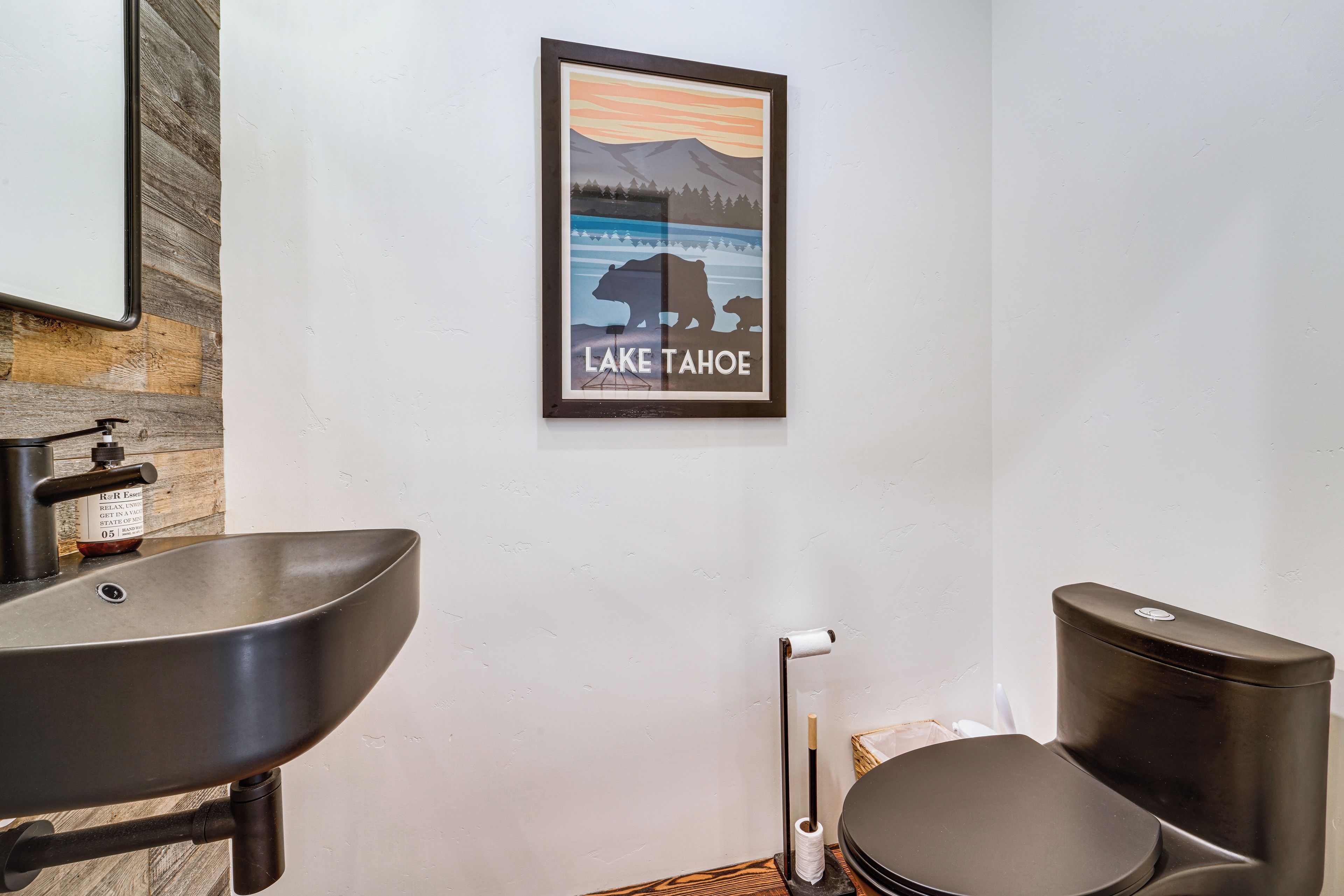 A bathroom with a sink, toilet, and a framed picture of Lake Tahoe.