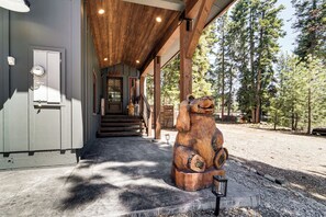 A wooden exterior with a bear sculpture, a covered entrance, and a concrete pathway leading to a building.