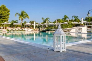 Una piscina con lettini e ombrelloni, circondata da palme.