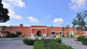 Ein Gebäude mit roter Fassade, einem Bogenportal und einem Innenhof mit Grünflächen.
