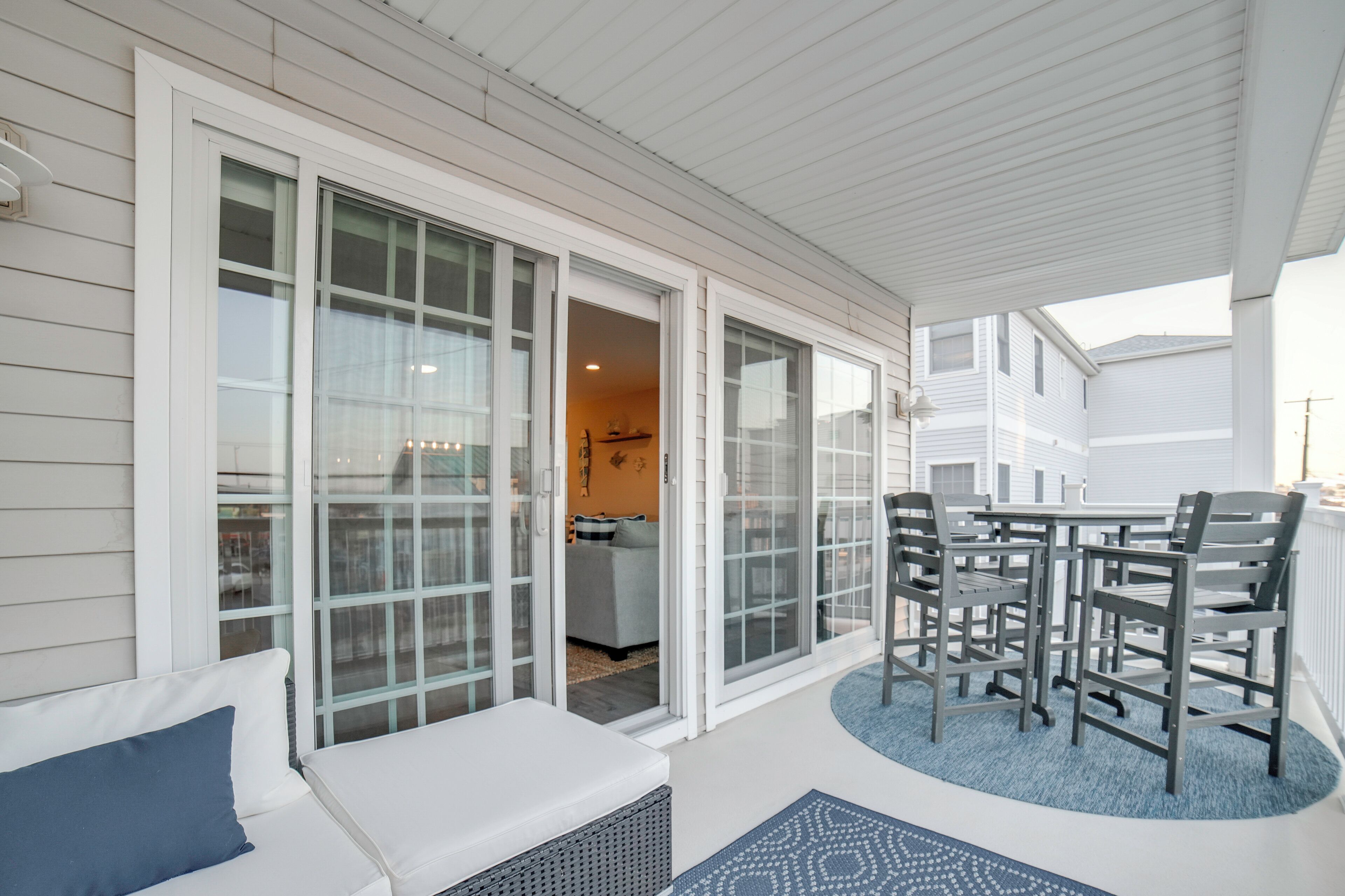 A covered outdoor area with a white exterior, a seating area with a bench and chairs, and a view into the adjacent living space.
