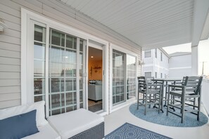 Ein überdachter Außenbereich mit weißer Fassade, ausgestattet mit einer Sitzgelegenheit, bestehend aus einer Bank und Stühlen, und Blick in den angrenzenden Wohnraum.