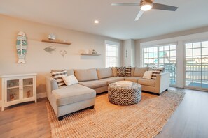 Ein Wohnzimmer mit Ecksofa, Hocker und Wandbildern.