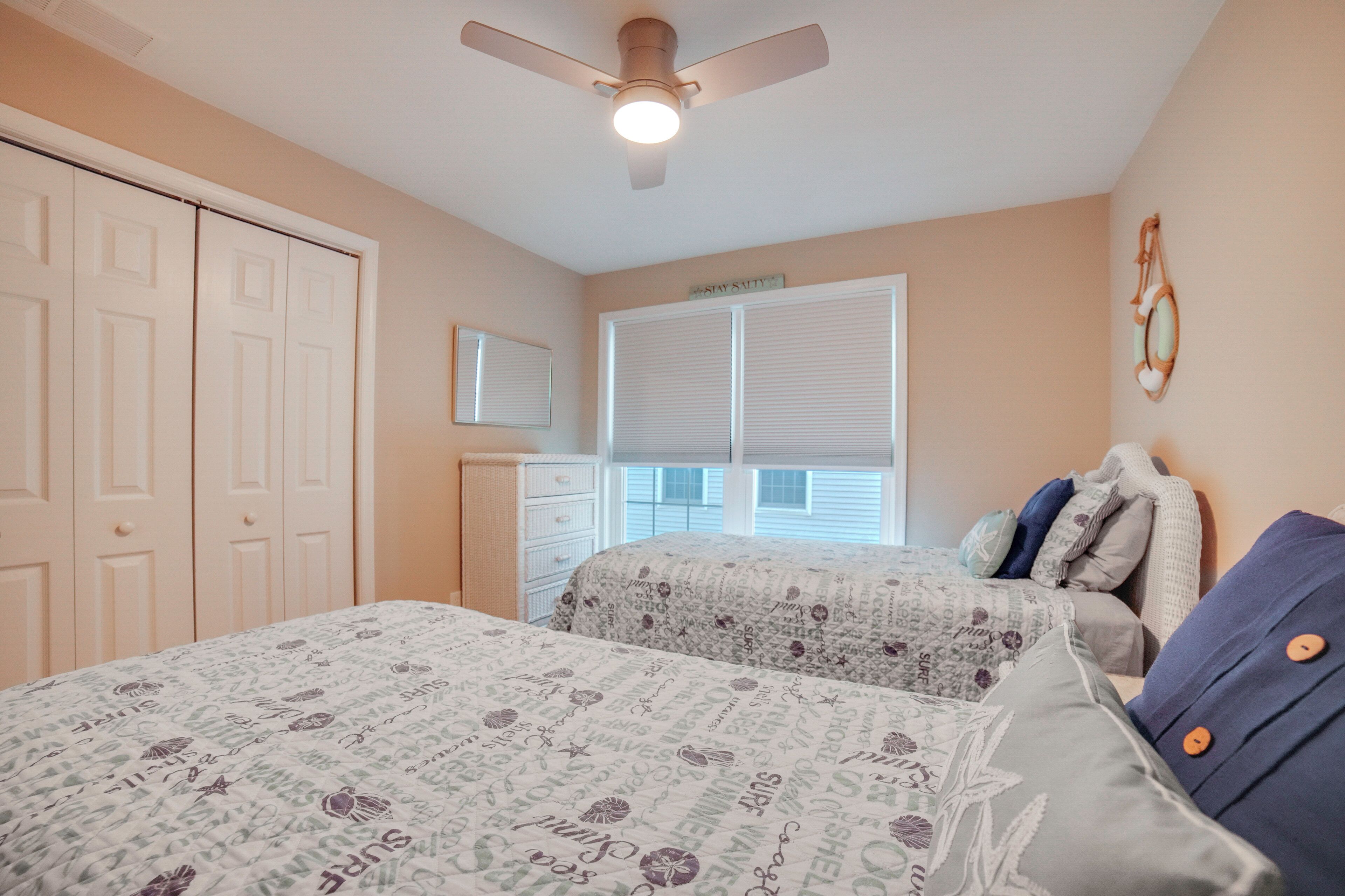 Une chambre avec deux lits, un ventilateur de plafond, une fenêtre avec des stores et une porte.
