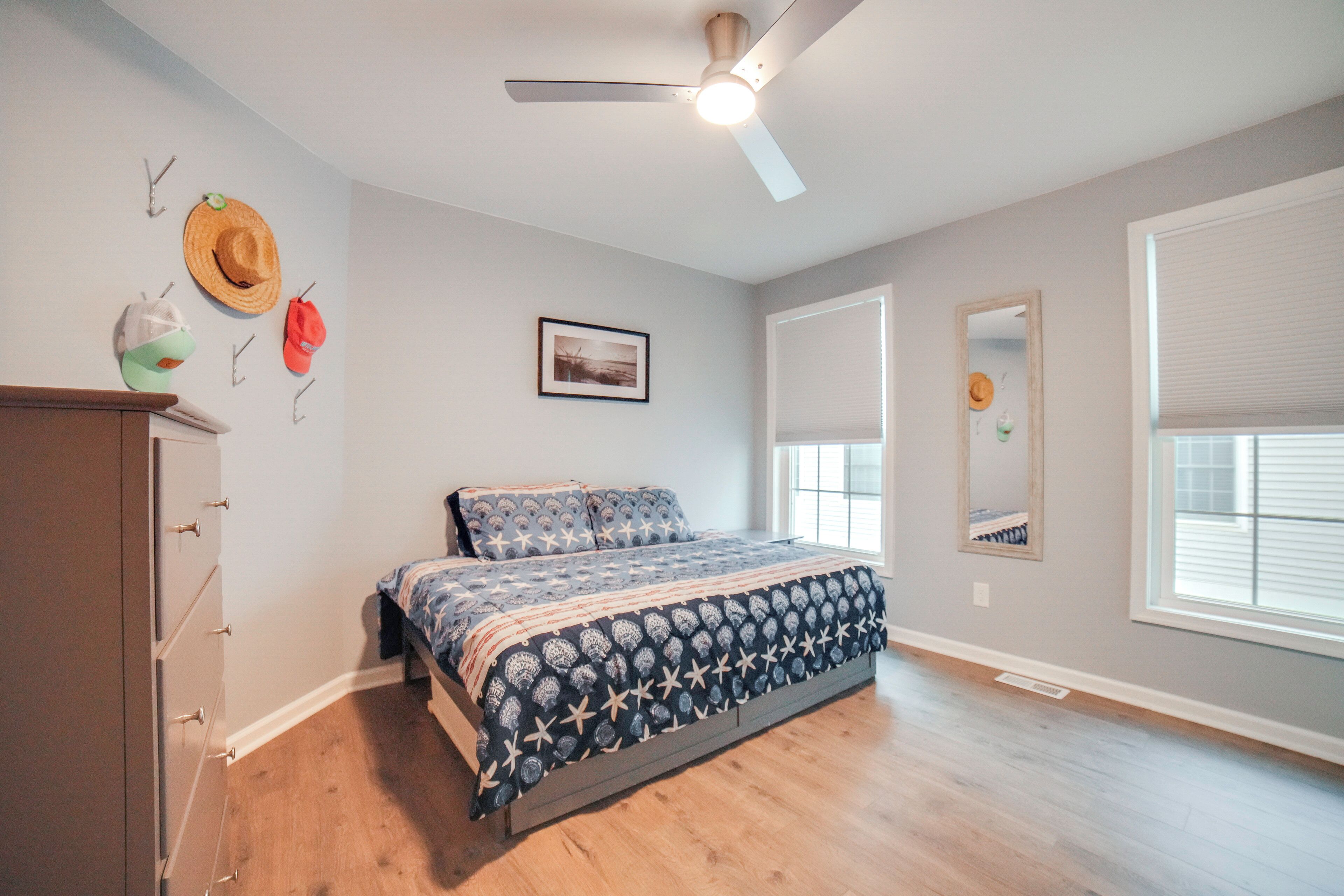 A bedroom with a bed, a ceiling fan, a dresser, a window, and wall decorations.