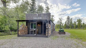 Tunnelmallinen, maalaishenkinen puurakennus, jonka yläpuolella on kyltti, jossa lukee »SALOON». Sen edessä on kivinen takka, pöytä ja tuoleja.
