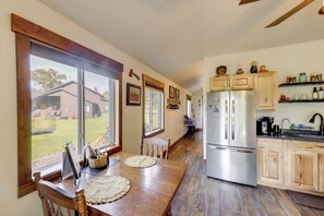 A kitchen with wooden cabinets, a stainless steel refrigerator, and a dining table with placemats. - On the Flathead River! Rustic Saloon-themed Cabin (Columbia Falls)