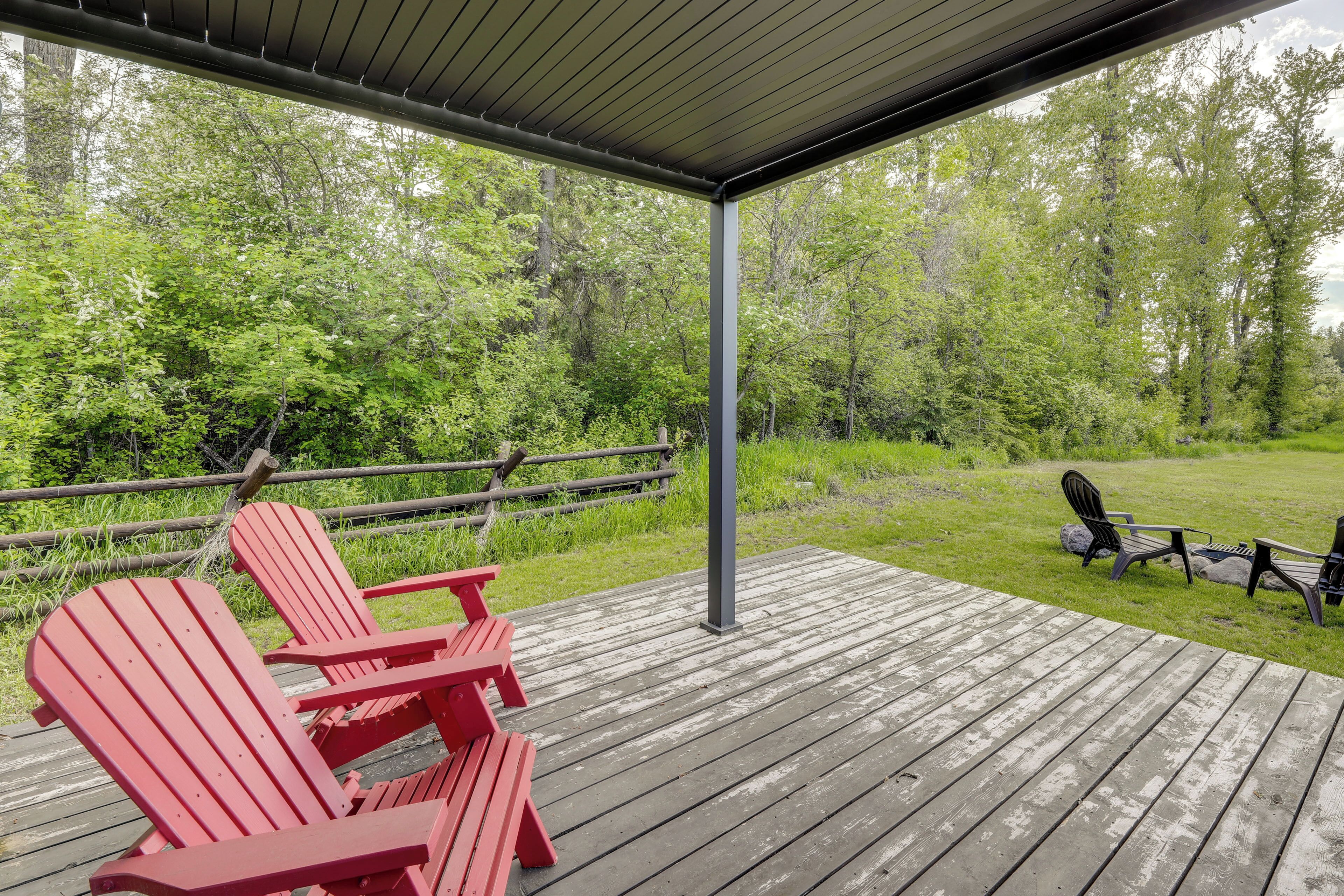 A wooden deck with red Adirondack chairs and a table, overlooking a grassy area with trees.
