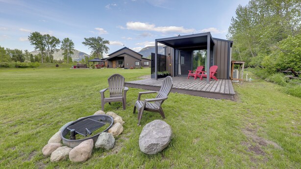Moderni ulkoterrassi, jossa on kaksi Adirondack-tyylistä tuolia, nuotiopaikka ja katettu oleskelualue.
