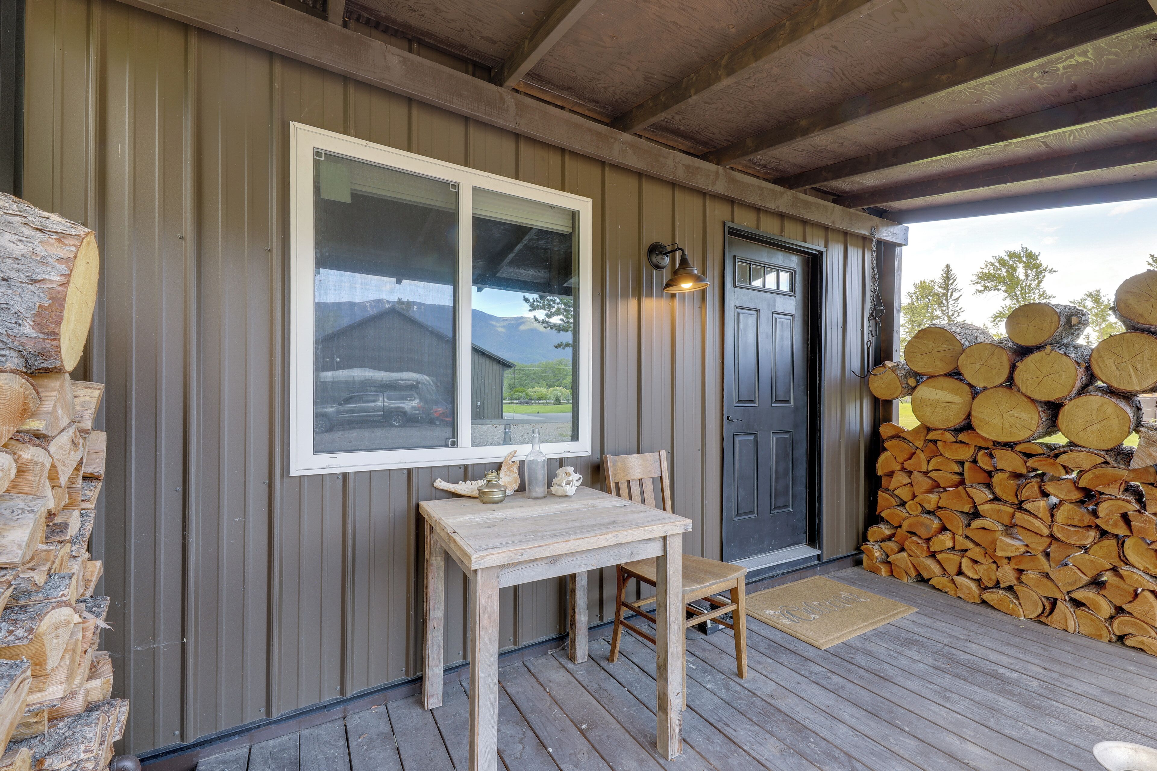 A wooden deck with a table and chair, a window, a door, and a stack of firewood.